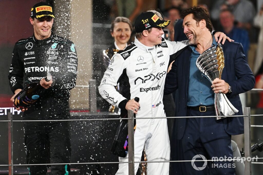 George Russell, Mercedes-AMG F1 Team, Brad Pitt, and Javier Bardem film a scene for an F1 movie on the podium.